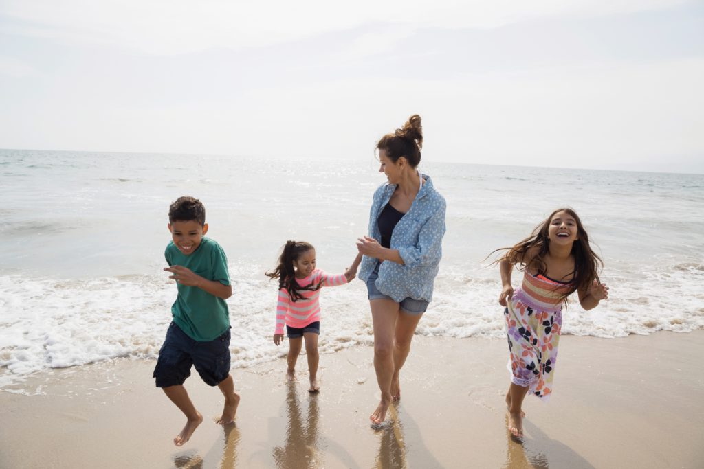 Family running along ocean surf on sunny beach
