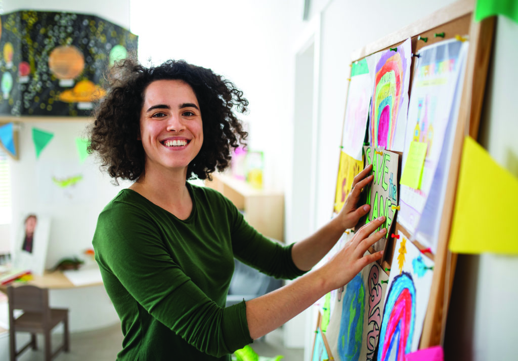 Profesor pegando carteles y dibujos en el tablón de anuncios de la escuela.