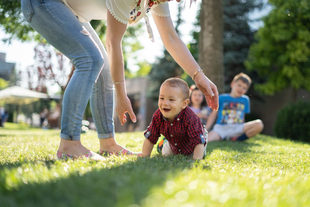 A baby crawling across grass to a care taker
